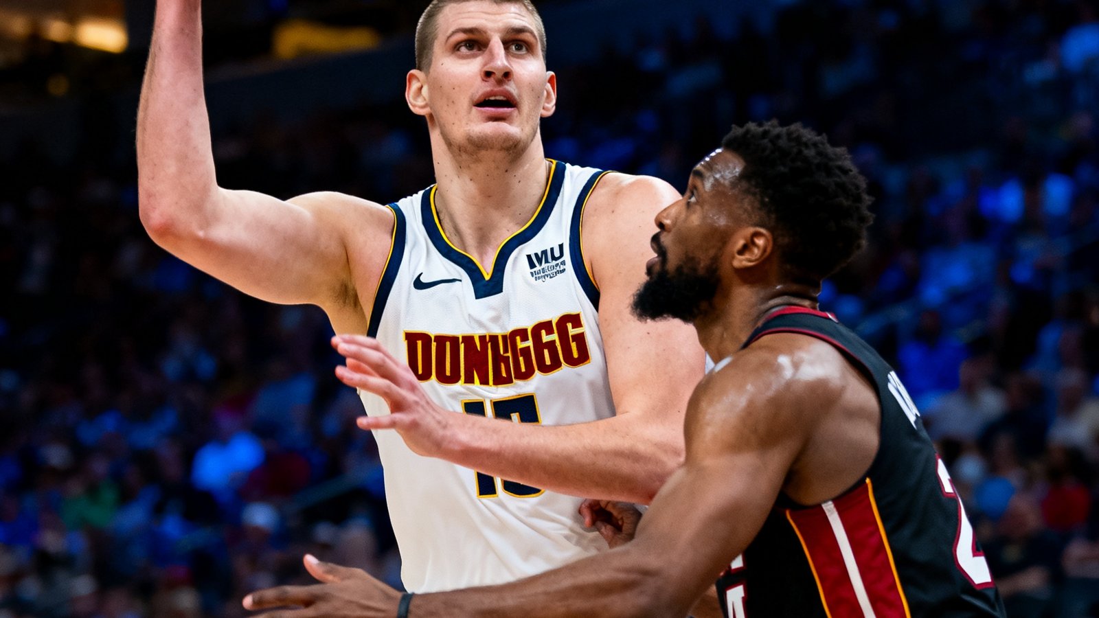 NBA总决赛中丹佛掘金队约基奇在篮下持球面对热火队防守的精彩画面，球场灯光聚焦在约基奇身上